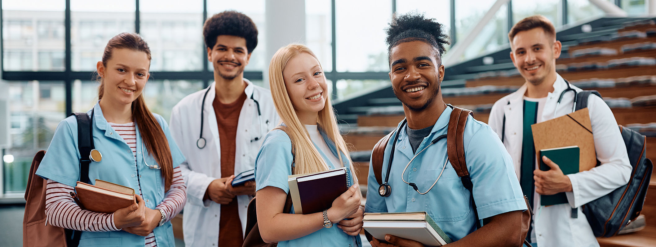 Gruppe von jungen Medizinstudierenden und Ärzten in Krankenhausflur mit Büchern und Kitteln